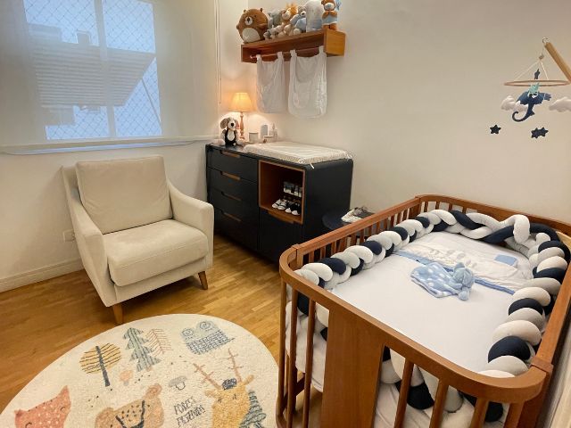 Quarto de bebê com tons de azul e branco com um berço em madeira, uma cômoda azul marinho e uma poltrona branca e um tapete infantil decorativo